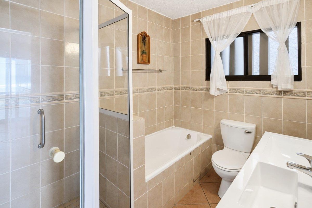 A functional bathroom featuring a shower enclosure, built-in bathtub, toilet, and a double vanity with tiled finishes throughout.