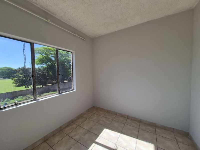 A vacant bedroom featuring neutral walls, tiled flooring, and a large window providing natural light and exterior views.