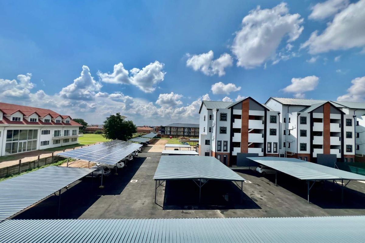 An elevated view of the apartment complex grounds, featuring paved parking areas with covered carports and solar panel installations.