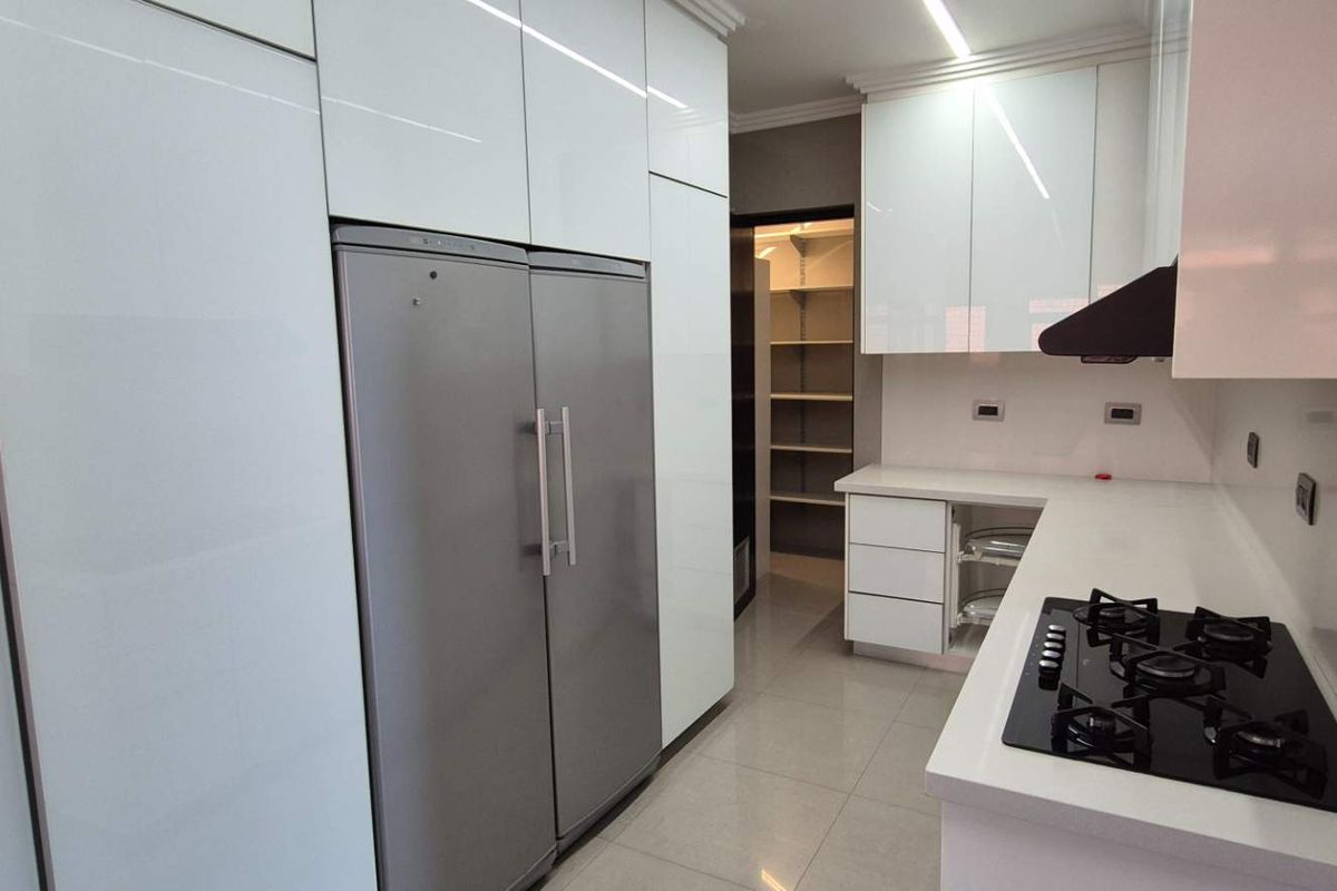 Modern kitchen featuring high-gloss white cabinetry, stone countertops, a built-in gas cooktop, and an adjacent walk-in pantry with shelving.