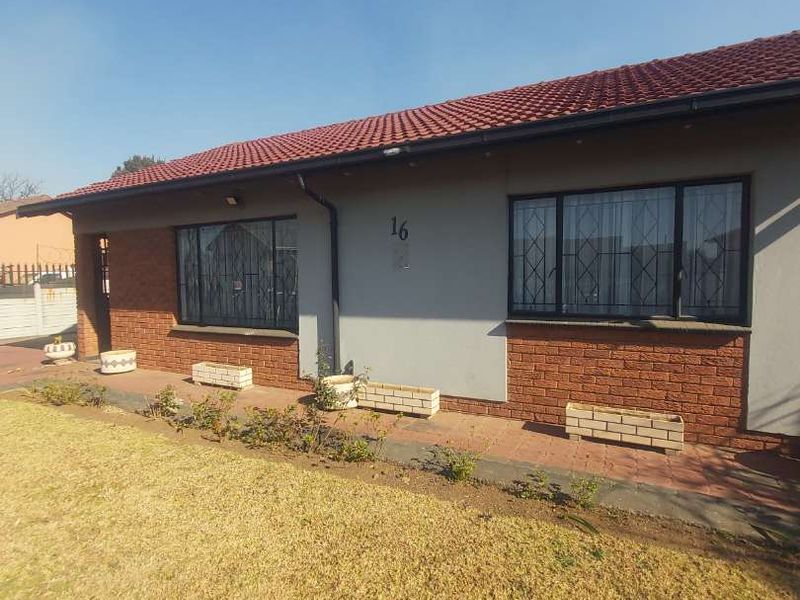 Front elevation of a single-story house featuring a tiled roof, brick accents, and security bars on the windows.