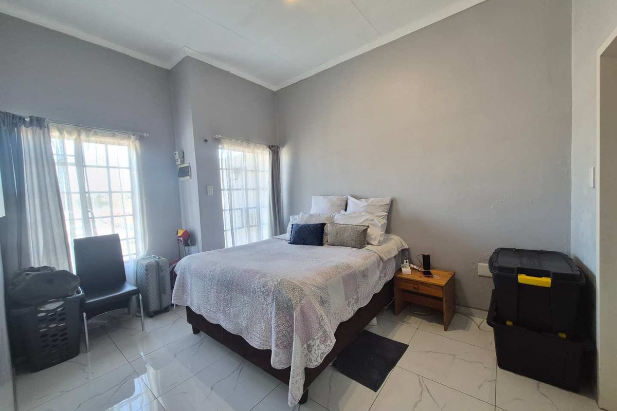 A bedroom featuring white tiled flooring, neutral grey walls, and dual windows allowing natural light into the space.