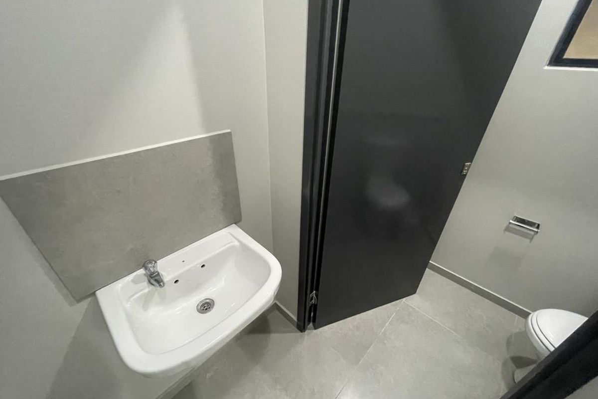 A modern guest bathroom featuring a wall-mounted basin with a tiled splashback, grey floor tiles, and a dark door leading to the toilet area.