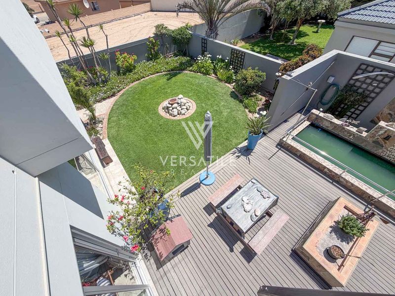 Elevated view of a well-maintained rear garden featuring a swimming pool, timber decking, and a circular lawn area with stone landscaping.