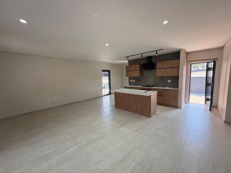 Modern open-plan living area featuring a sleek kitchen with a central island, wood-finish cabinetry, and large format floor tiles.