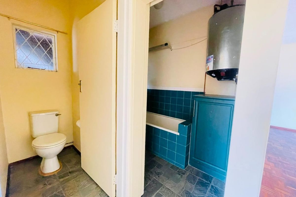 A functional bathroom area featuring a toilet, bathtub with tiled surround, and an exposed electric water heater unit.