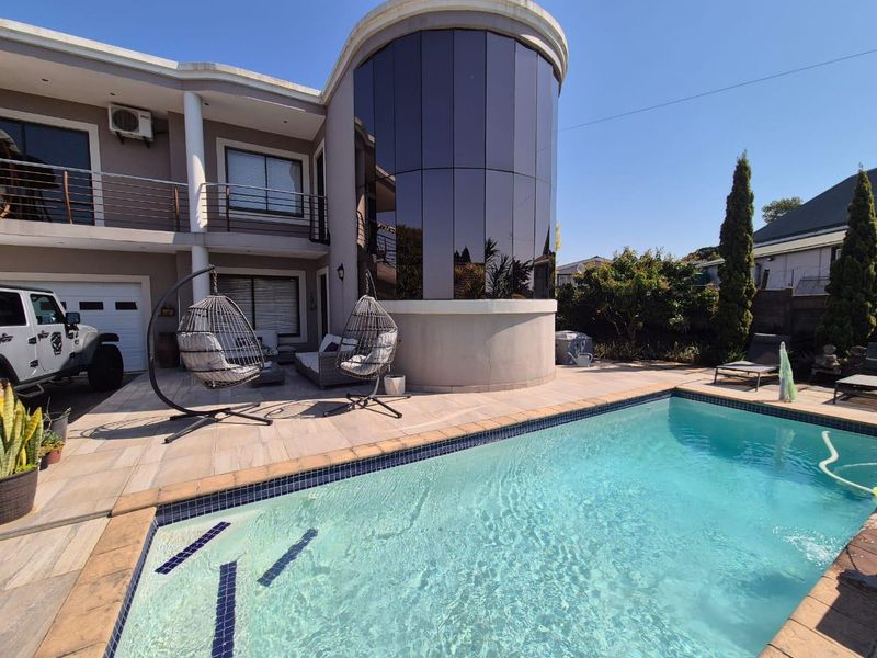 Rear exterior view featuring a swimming pool, tiled patio area, and a distinctive curved glass architectural feature on the main building facade.