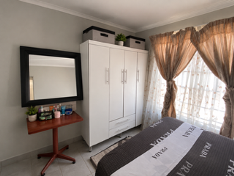 A bedroom featuring a white built-in wardrobe, tiled flooring, and neutral wall finishes, providing a functional and well-lit living space.