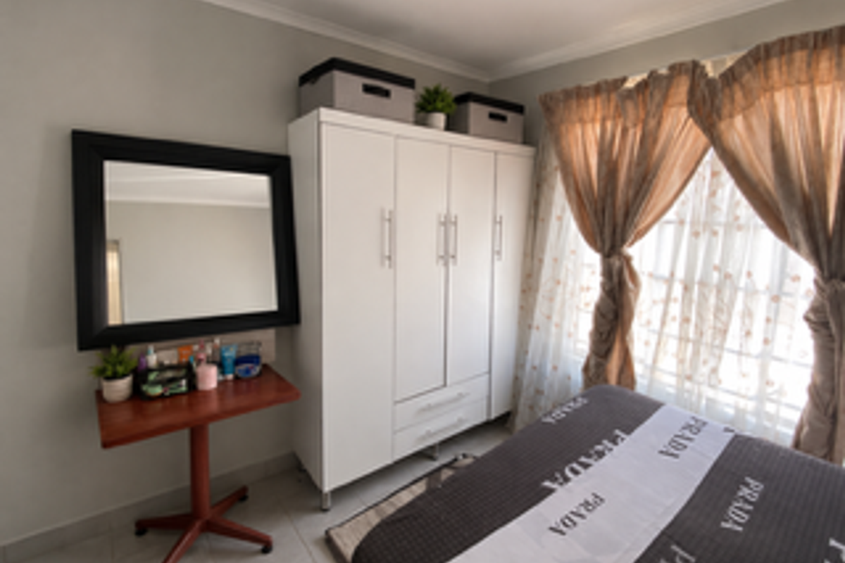 A bedroom featuring a white built-in wardrobe, tiled flooring, and neutral wall finishes, providing a functional and well-lit living space.