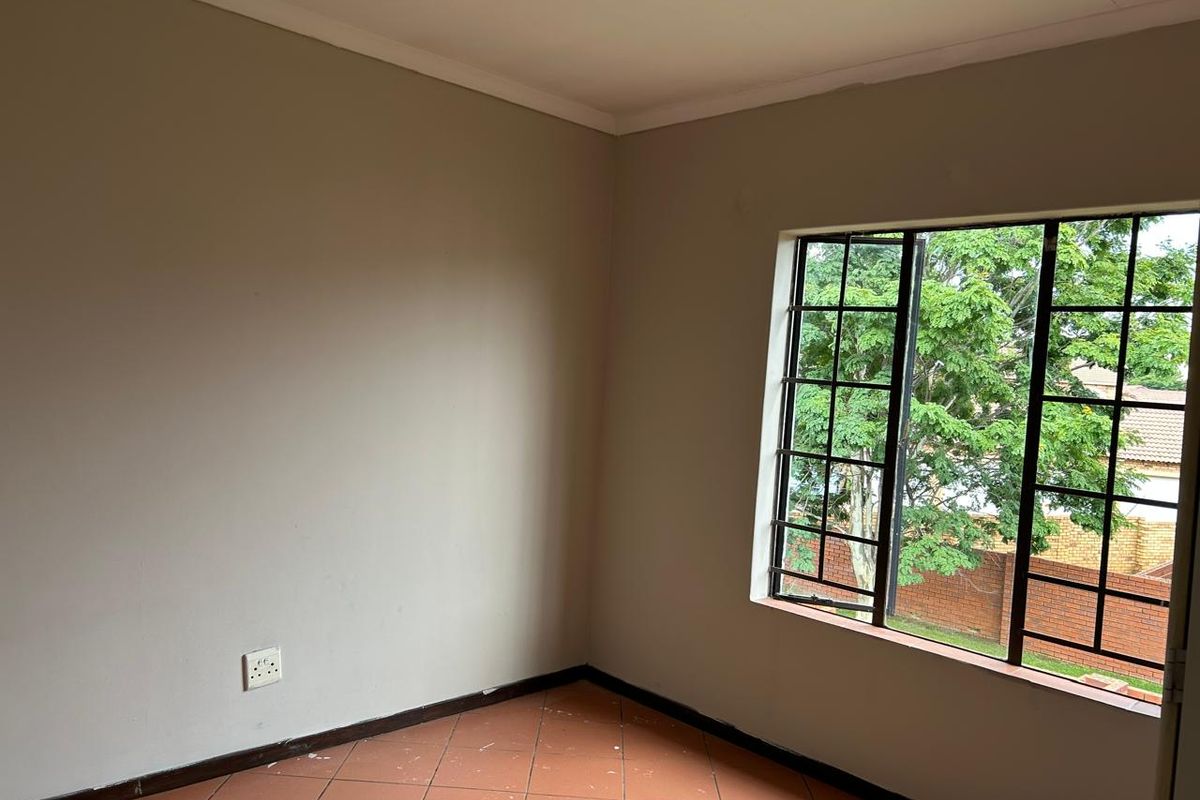 An empty bedroom featuring tiled flooring, neutral walls, and a steel-framed window overlooking the exterior.
