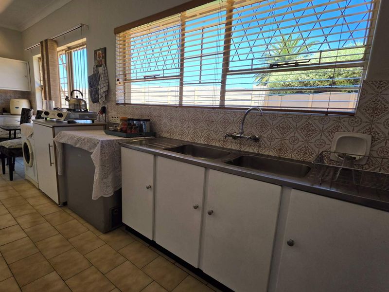 A functional kitchen featuring a double stainless steel sink, tiled backsplash, and ample built-in cabinetry, offering a practical layout with natural light.