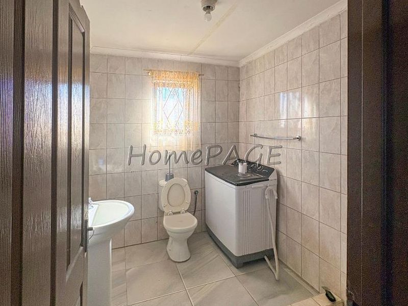 A functional laundry and bathroom space featuring tiled walls and floors, a pedestal basin, and a built-in tiled shower base.
