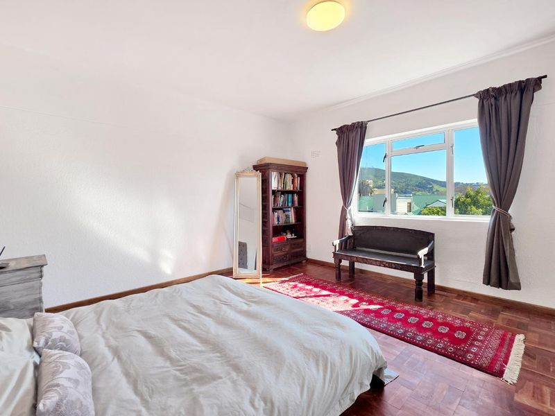 A bright bedroom featuring classic parquet flooring and a large window with scenic views, offering a comfortable and well-lit living space.