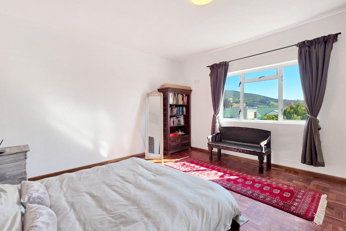 A bright bedroom featuring classic parquet flooring and a large window with scenic views, offering a comfortable and well-lit living space.