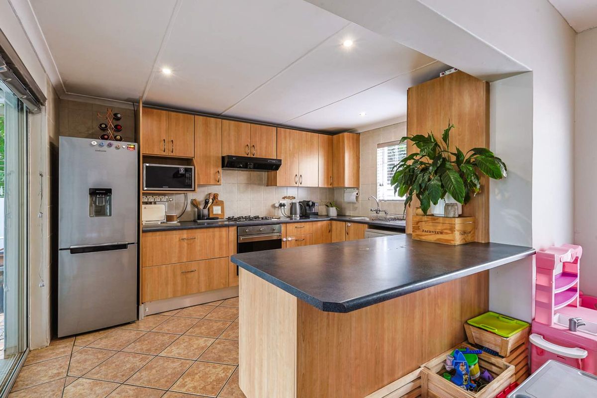 A functional kitchen featuring wood-look cabinetry, a breakfast bar, tiled flooring, and built-in appliances including an oven, hob, and extractor fan.
