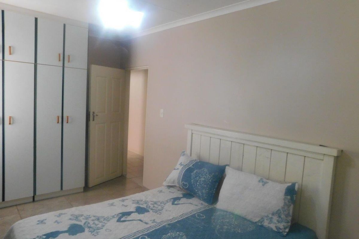 A bedroom featuring built-in cupboards, tiled flooring, and a ceiling fan, providing a functional and neutral living space.