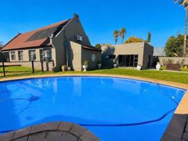 A well-maintained backyard featuring a large swimming pool with solar heating, paved surrounds, and a spacious lawn area adjacent to the main residence.