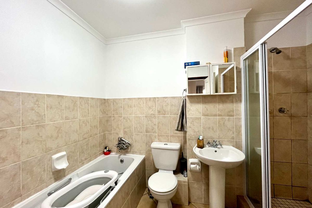 A functional bathroom featuring a bathtub, separate shower enclosure, pedestal sink, and toilet with neutral wall and floor tiling.