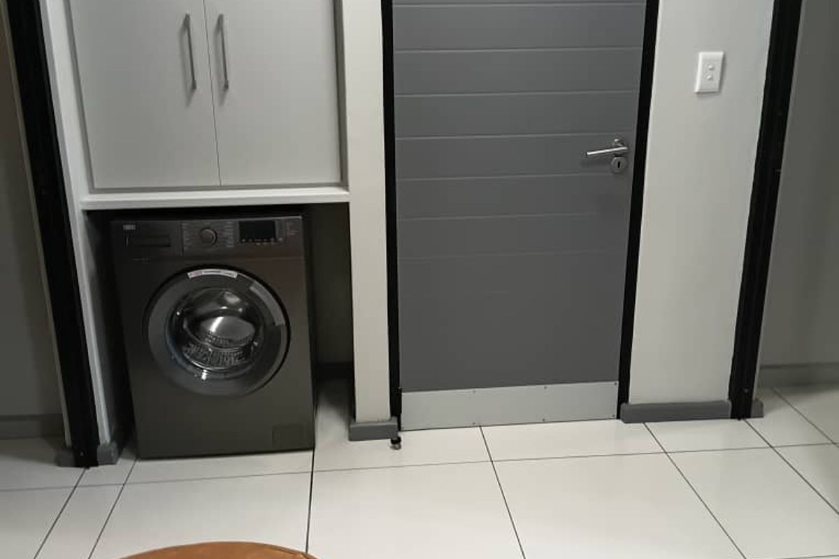 A functional laundry area featuring built-in cabinetry for storage and tiled flooring, integrated into the apartment layout.