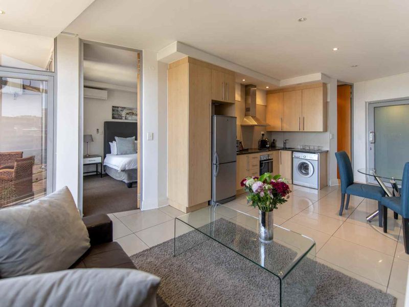 Modern open-plan living area featuring a compact kitchen with built-in cabinetry, tiled floors, and direct access to a private balcony.