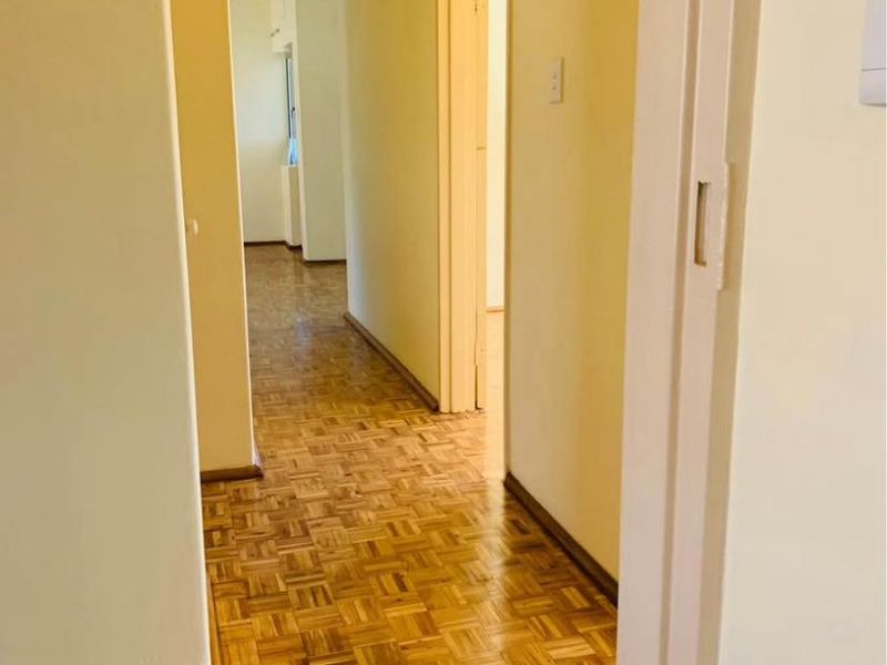 A vacant hallway featuring well-maintained parquet flooring and neutral wall finishes, providing access to adjacent rooms within the apartment.
