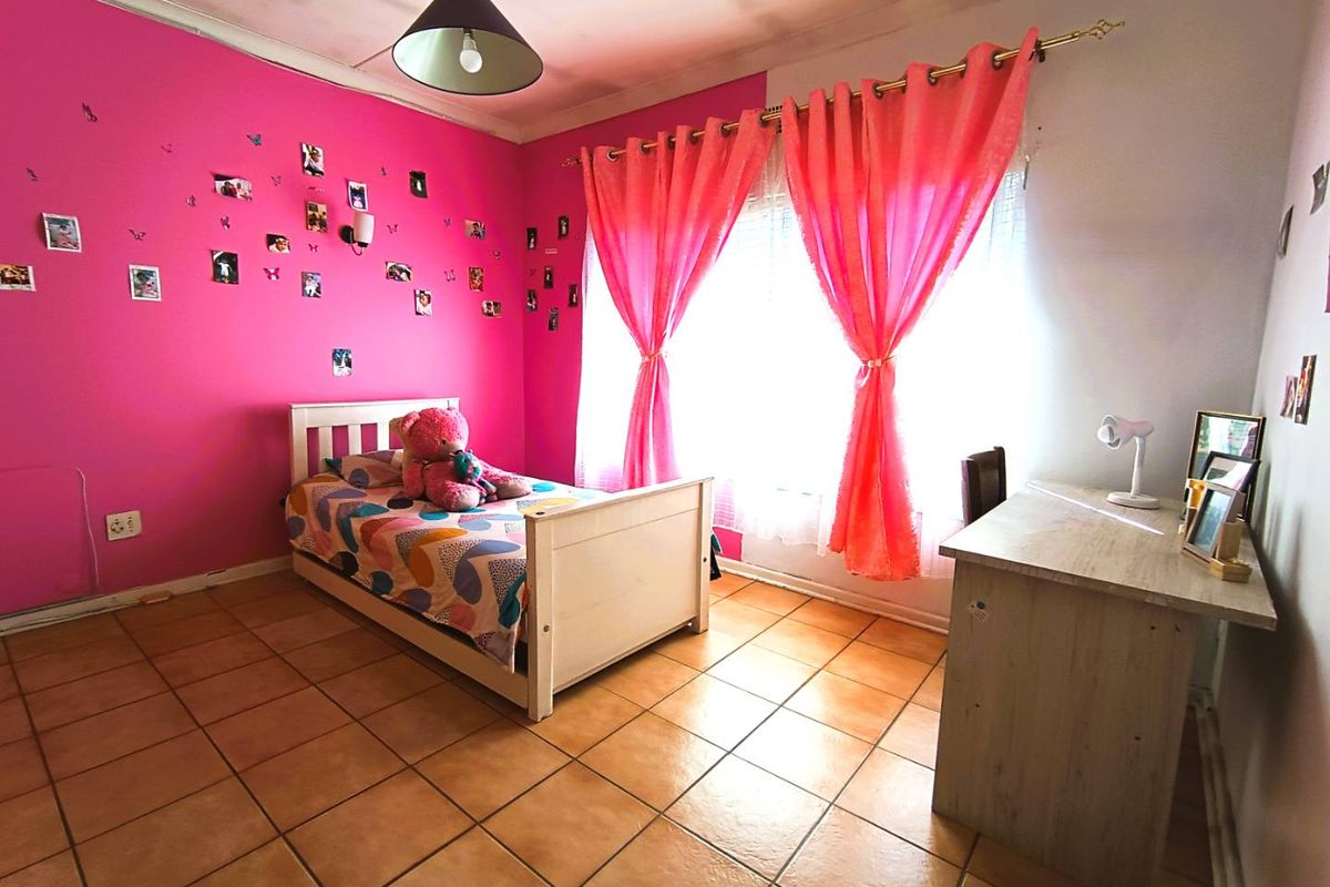 A bedroom featuring tiled flooring, a bright pink accent wall, and a large window with curtains, providing a functional living space.