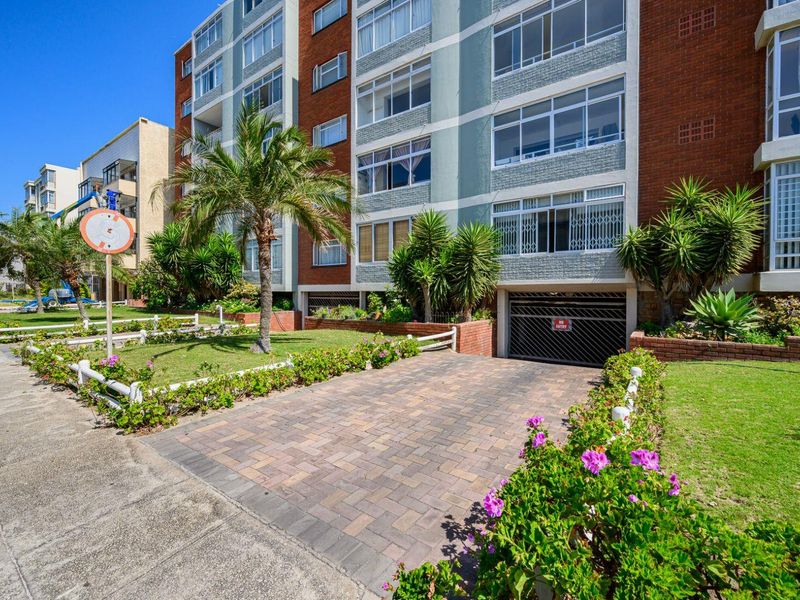 Front exterior view of a multi-story apartment building featuring a paved driveway, secure basement parking access, and well-maintained landscaped garden areas.