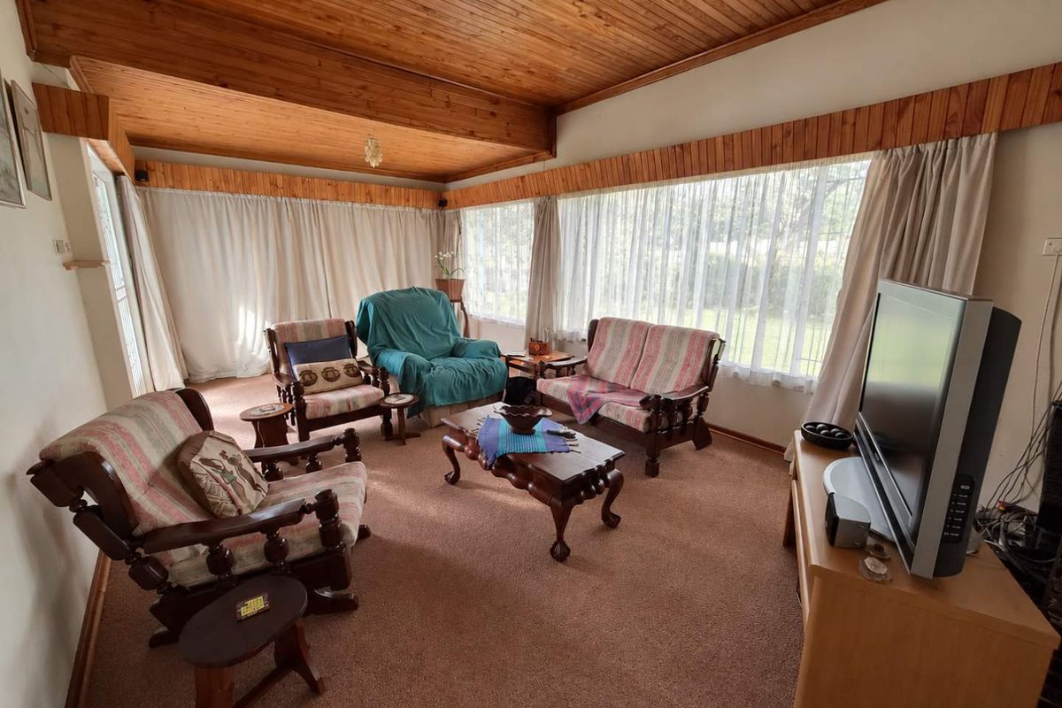 A cozy living room featuring a distinctive timber-clad vaulted ceiling, large windows allowing natural light, and fitted carpeting throughout.