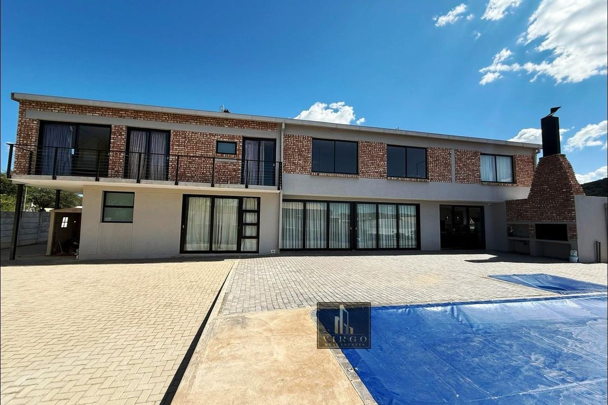Rear view of a two-story house featuring a brick facade, balcony, paved patio area, and a swimming pool with a built-in outdoor braai.