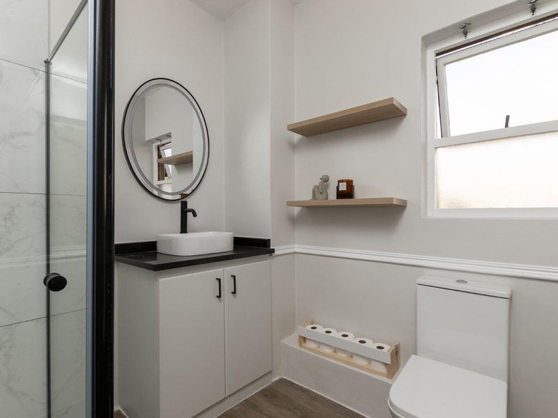 Modern bathroom featuring a vessel sink with black fixtures, a glass-enclosed shower, and floating wooden shelves.