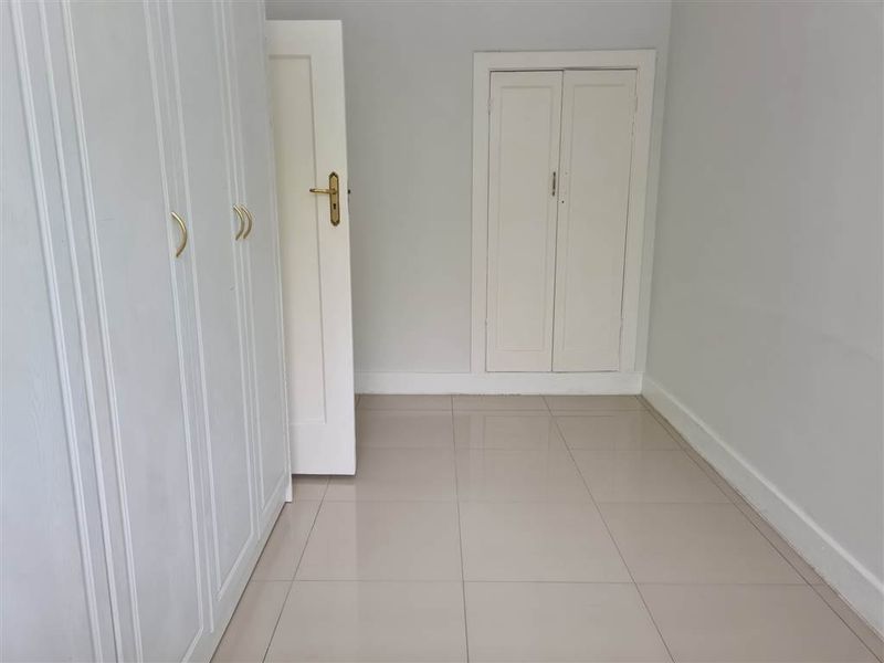 A clean, empty bedroom featuring neutral tiled flooring and ample built-in cupboard storage space.