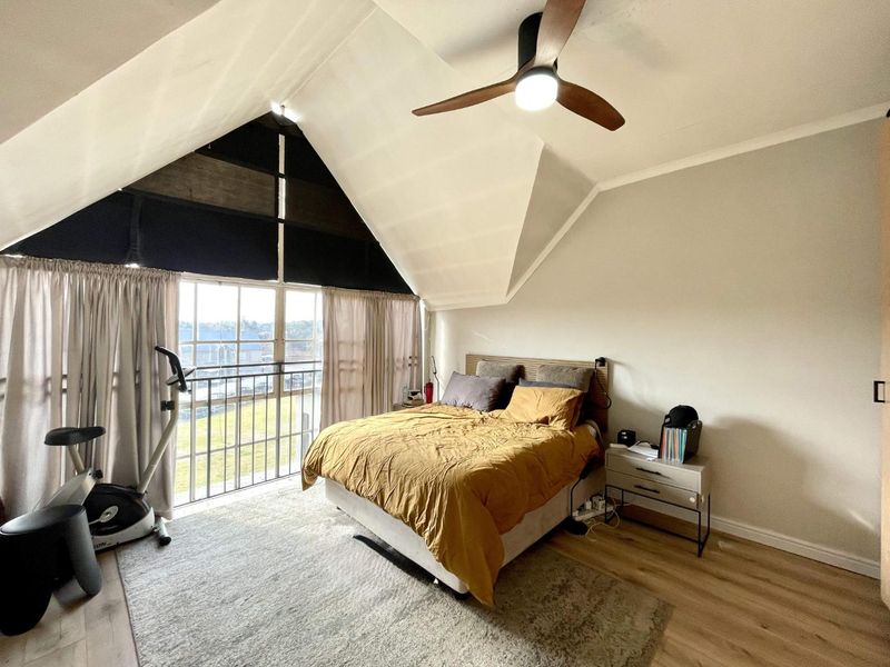 Spacious bedroom featuring a high vaulted ceiling, modern ceiling fan, laminate flooring, and large windows with access to a private balcony.