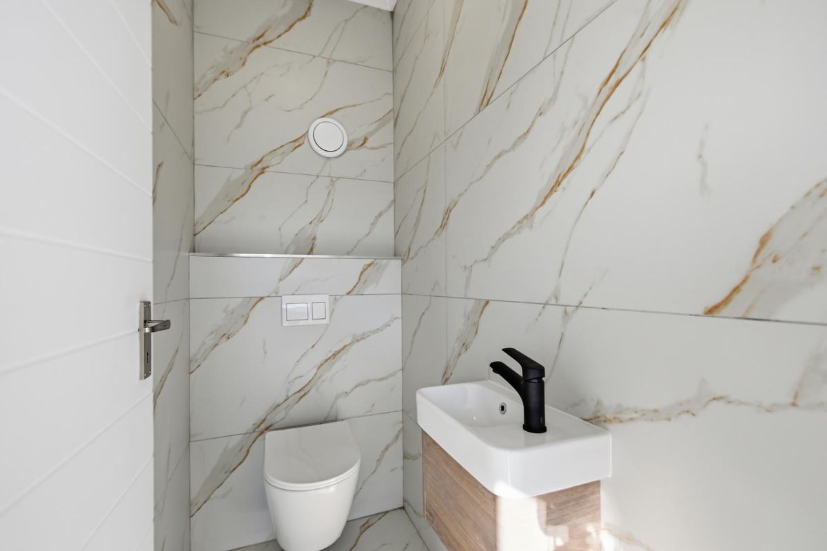 Modern guest bathroom featuring floor-to-ceiling marble-look tiles, a wall-hung toilet with concealed cistern, and a compact vanity basin with a matte black mixer tap.
