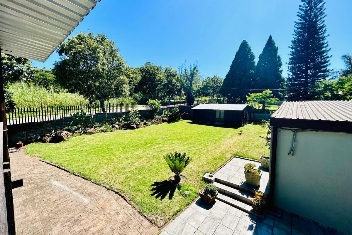 A spacious rear garden featuring a manicured lawn, paved patio area, and a detached outbuilding, enclosed by perimeter fencing.