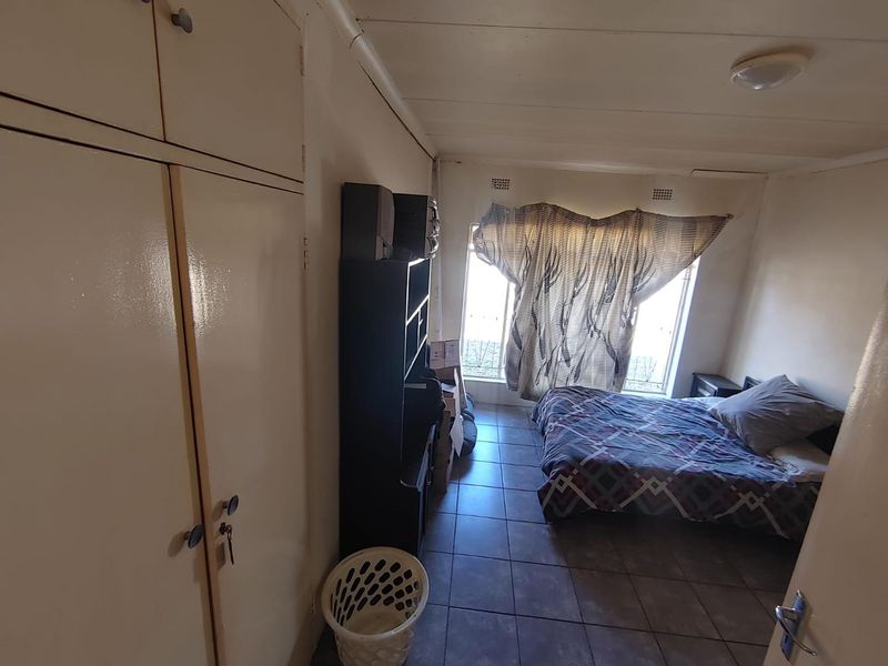 A functional bedroom featuring built-in cupboards, tiled flooring, and security bars on the windows. The space requires cosmetic updates to improve its overall condition.