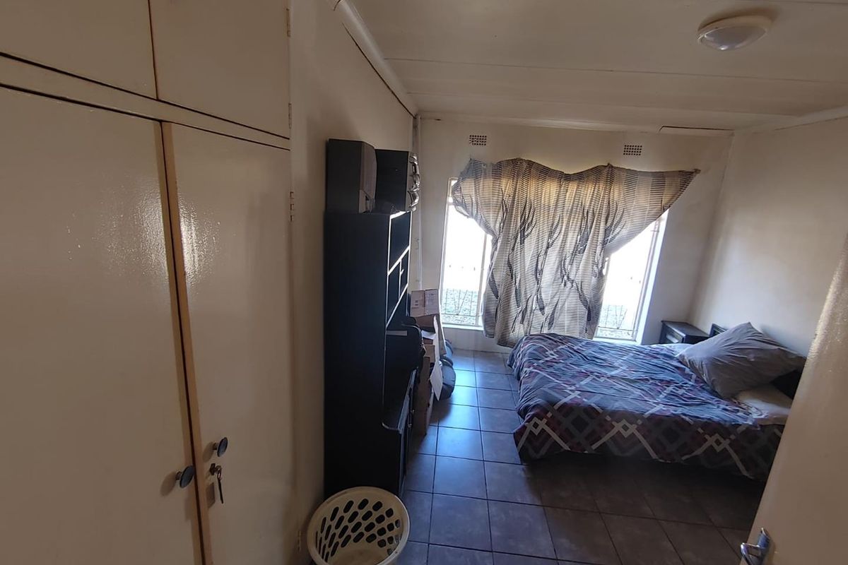 A functional bedroom featuring built-in cupboards, tiled flooring, and security bars on the windows. The space requires cosmetic updates to improve its overall condition.