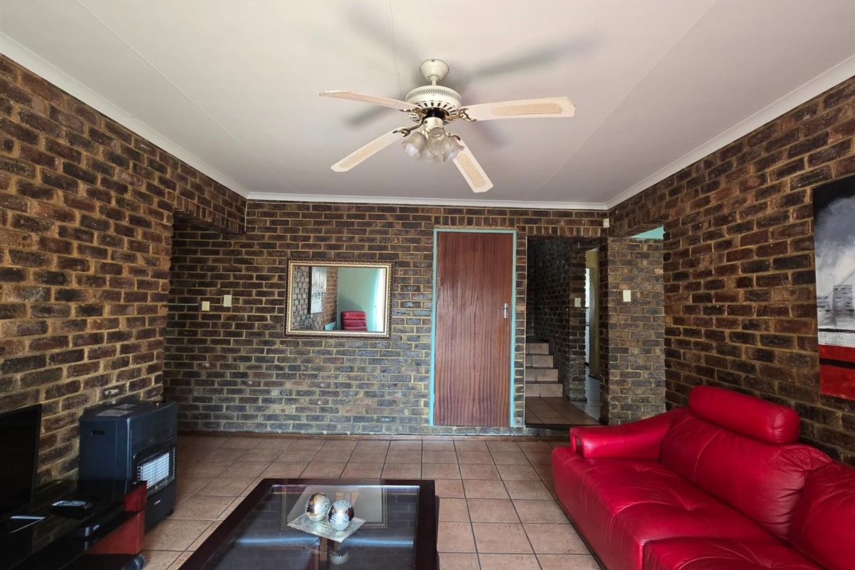 A living room featuring exposed face-brick walls, tiled flooring, and a ceiling fan, providing a rustic and functional living space.