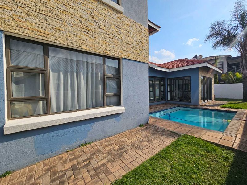 Rear exterior view featuring a swimming pool, paved patio area, and a multi-textured facade with stone cladding and blue painted plaster.