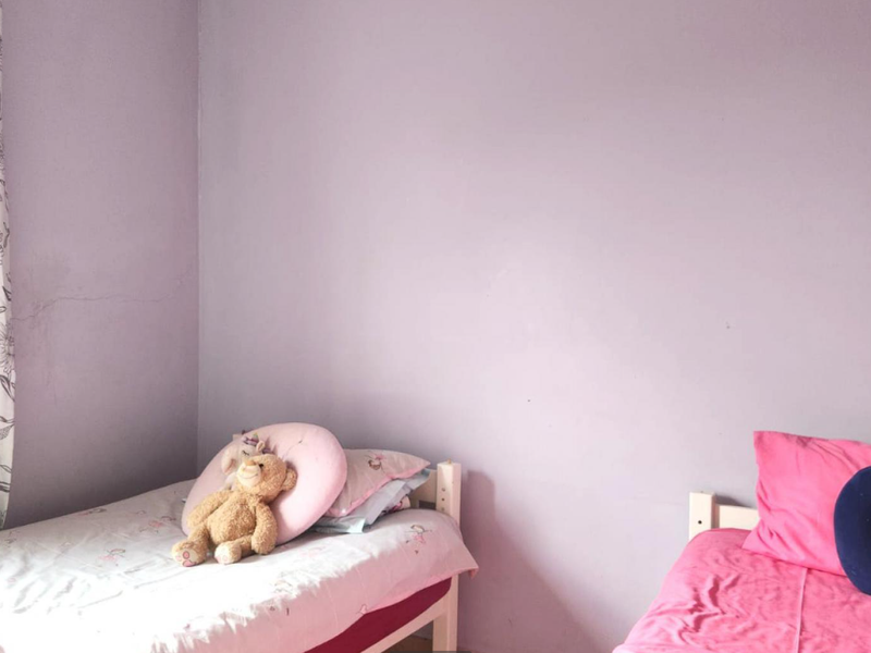 A bedroom featuring lavender-painted walls and visible hairline cracks, providing a blank canvas for potential updates and personalization.