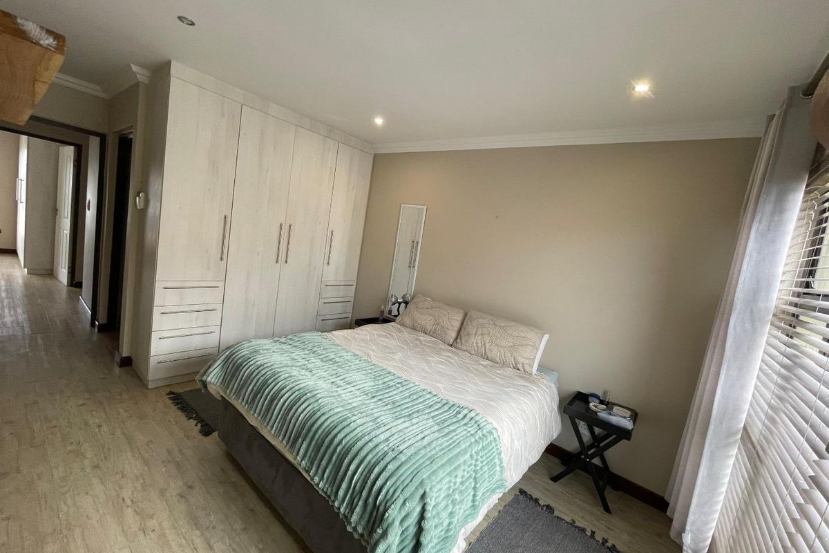 A well-maintained bedroom featuring built-in cupboards, recessed ceiling lighting, and light-toned laminate flooring.