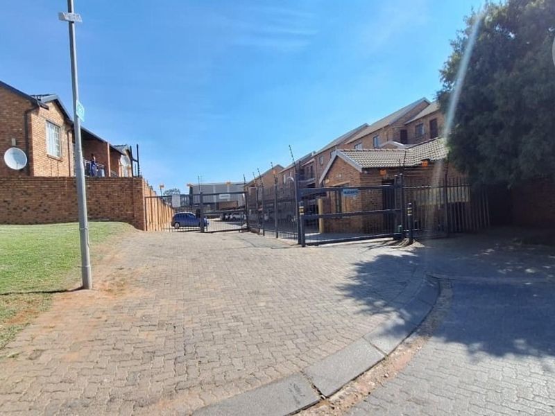 Street view of the apartment complex entrance featuring a paved driveway, secure gated access, and perimeter walling with electric fencing.