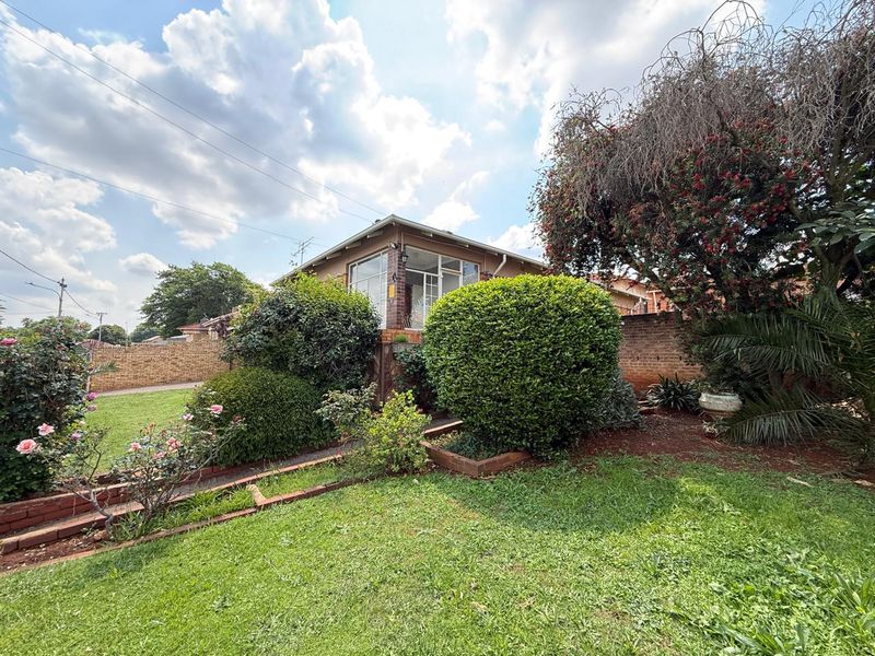 A view of the rear garden featuring established landscaping, brick boundary walls, and raised garden beds surrounding the property.