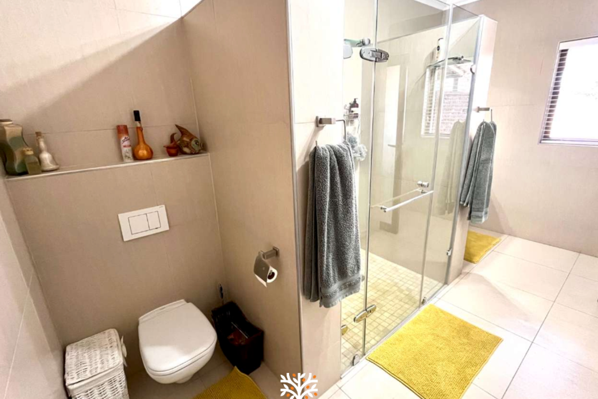 Modern bathroom featuring a wall-mounted toilet, a spacious glass-enclosed walk-in shower, and neutral floor-to-ceiling tiling.