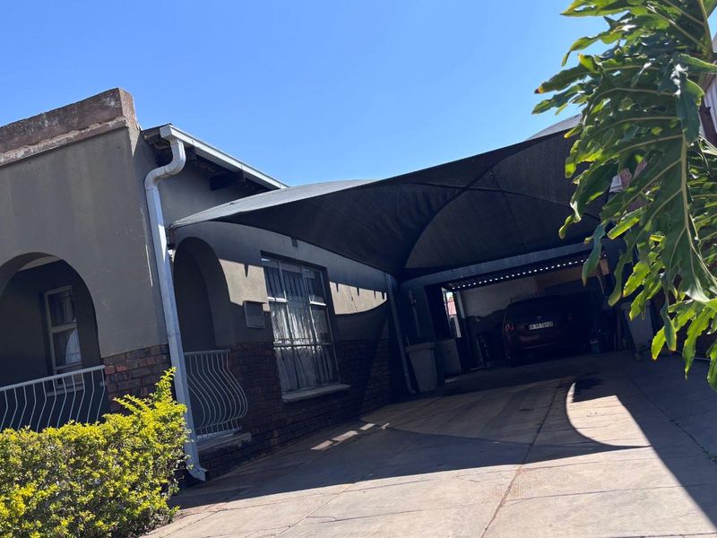 Front exterior view of the house featuring a paved driveway, a large shade sail structure, and an arched porch entrance.