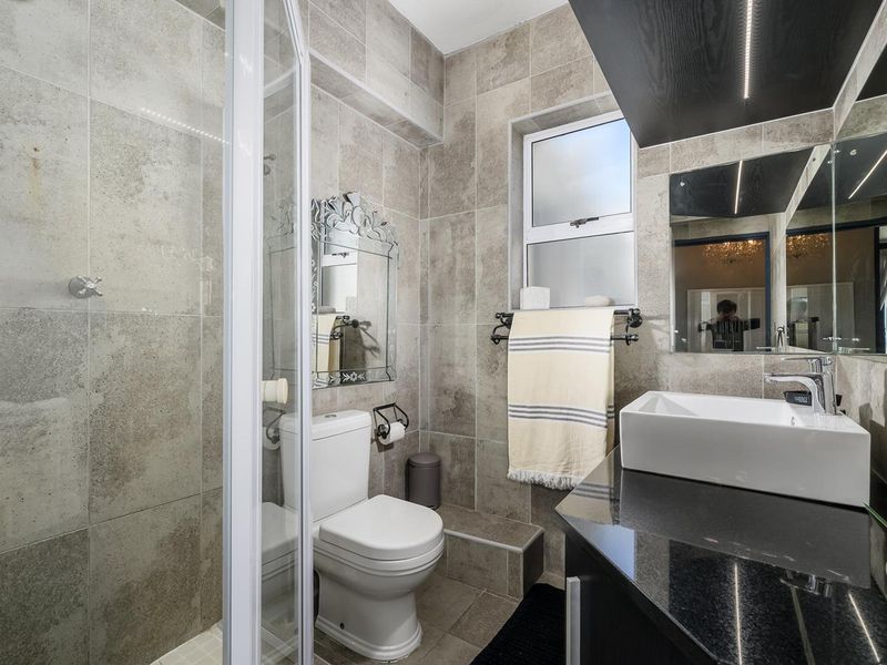 Modern bathroom featuring a glass shower enclosure, vessel sink on a granite vanity, and neutral floor-to-ceiling tiling.