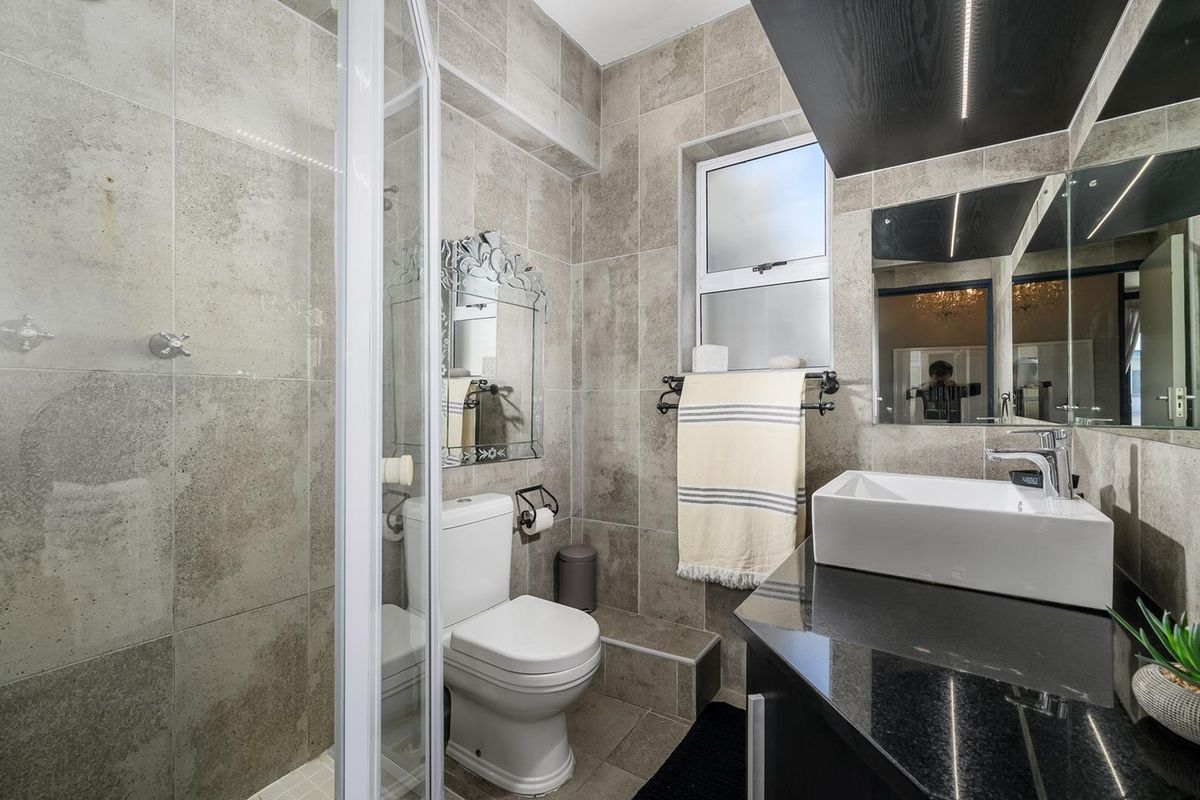 Modern bathroom featuring a glass shower enclosure, vessel sink on a granite vanity, and neutral floor-to-ceiling tiling.