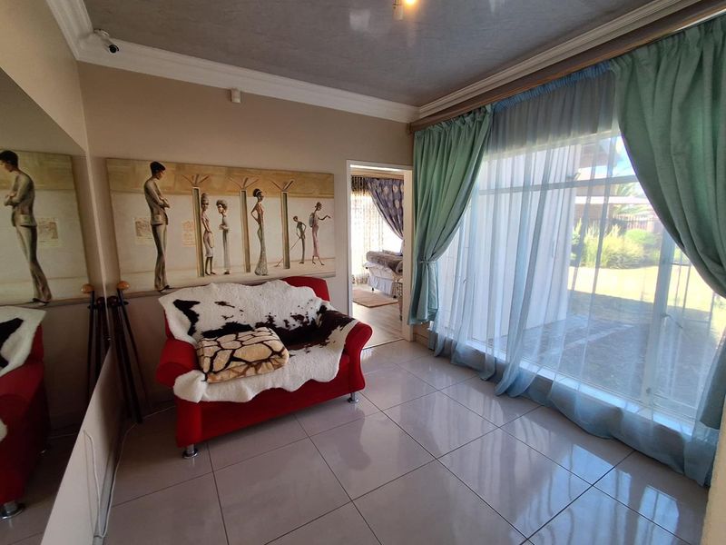 A living room featuring large sliding glass doors providing natural light, tiled flooring, and decorative ceiling coving, with access to an adjacent room.