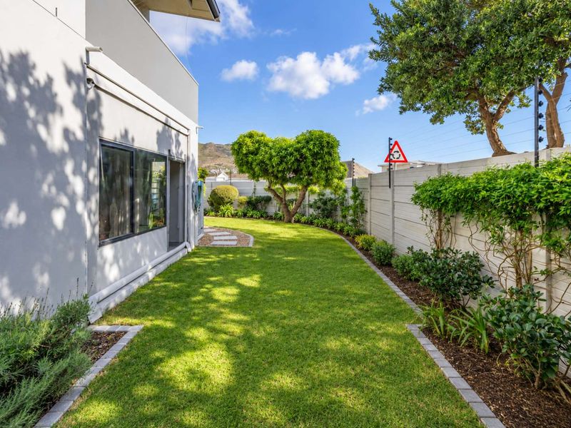 A well-maintained rear garden featuring a manicured lawn, landscaped garden beds with paved edging, and secure boundary walls with electric fencing.