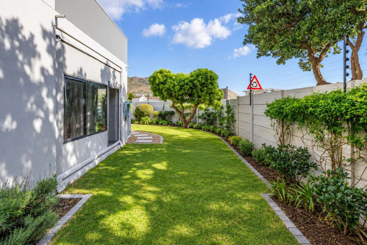 A well-maintained rear garden featuring a manicured lawn, landscaped garden beds with paved edging, and secure boundary walls with electric fencing.