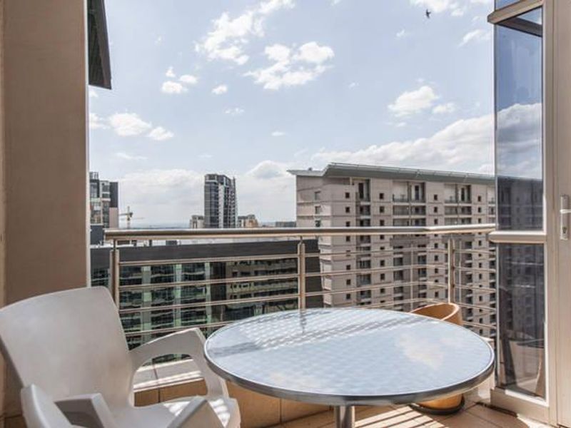 A private balcony featuring a stainless steel balustrade and tiled flooring, offering elevated urban views of the surrounding city skyline.